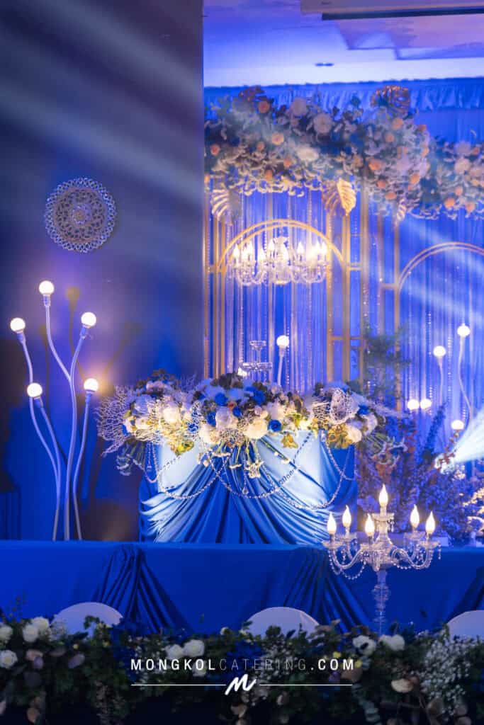 Elegant wedding reception decorated with blue drapes, floral arrangements, and chandeliers in Thailand.