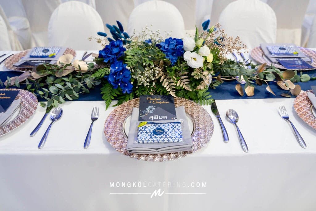 Colorful floral centerpiece with blue, white flowers, and greenery for elegant Thai event table setting.