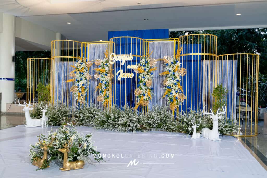 Elegant wedding backdrop with blue, gold, and white floral decor in Thailand.