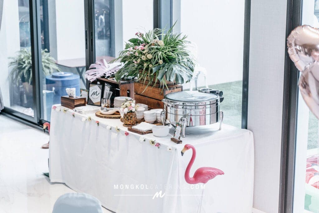 Colorful event buffet table with tropical decor in Thailand, featuring flowers, fruits, and catering setup.