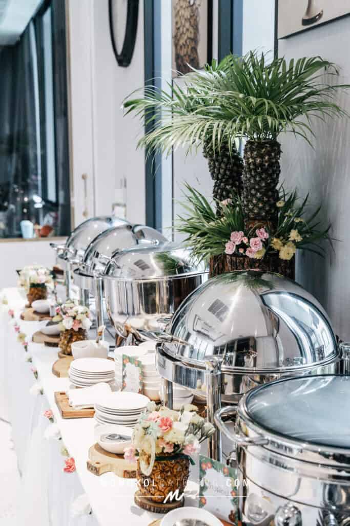 Elegant tropical event catering setup in Thailand with floral accents and stainless steel chafing dishes.