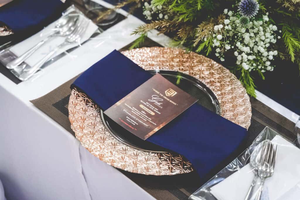 Elegant event table setting with blue napkin, gold charger plate, and floral centerpiece in Thailand.