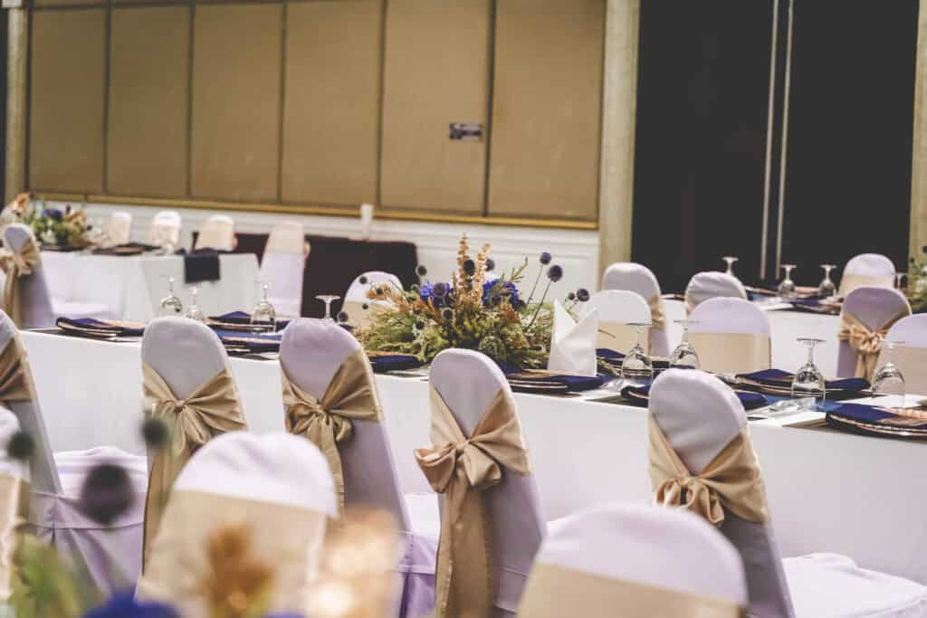 Elegant event table setup with white chair covers and gold bows in Thailand.
