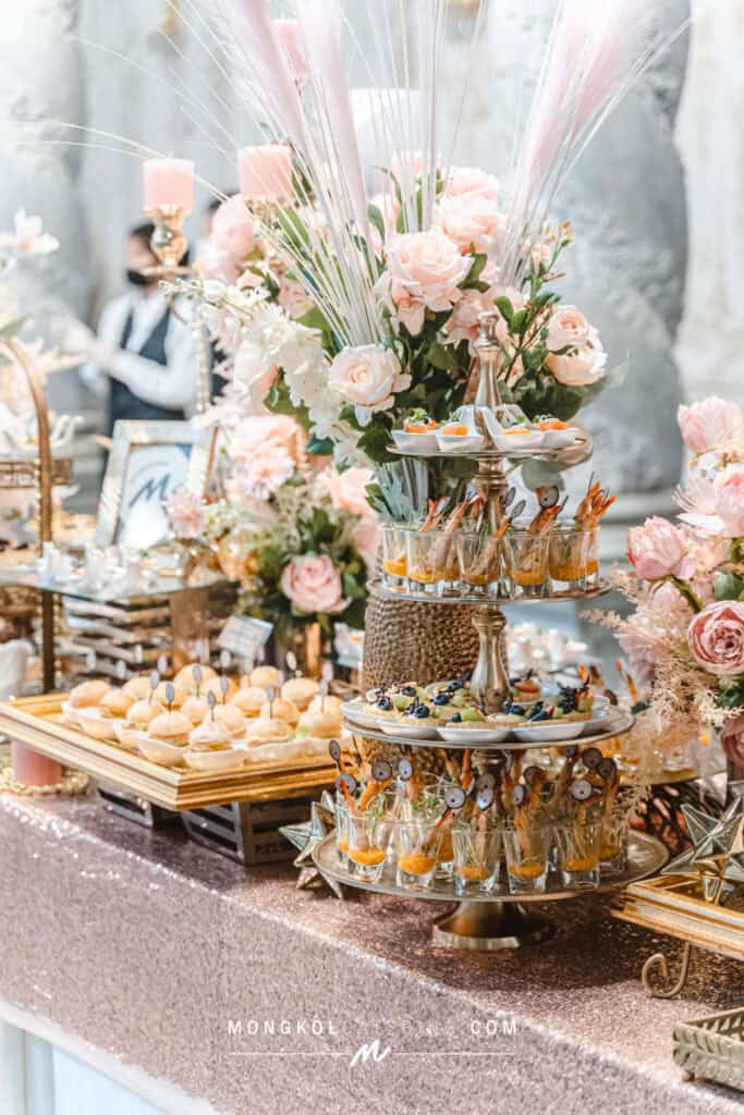 Elegant floral centerpiece with pastel roses and gourmet appetizers at Mongkol Catering event in Thailand.