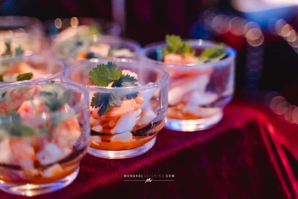 Bright Thai seafood salads in clear glass bowls with fresh herbs, served at a catering event in Thailand.