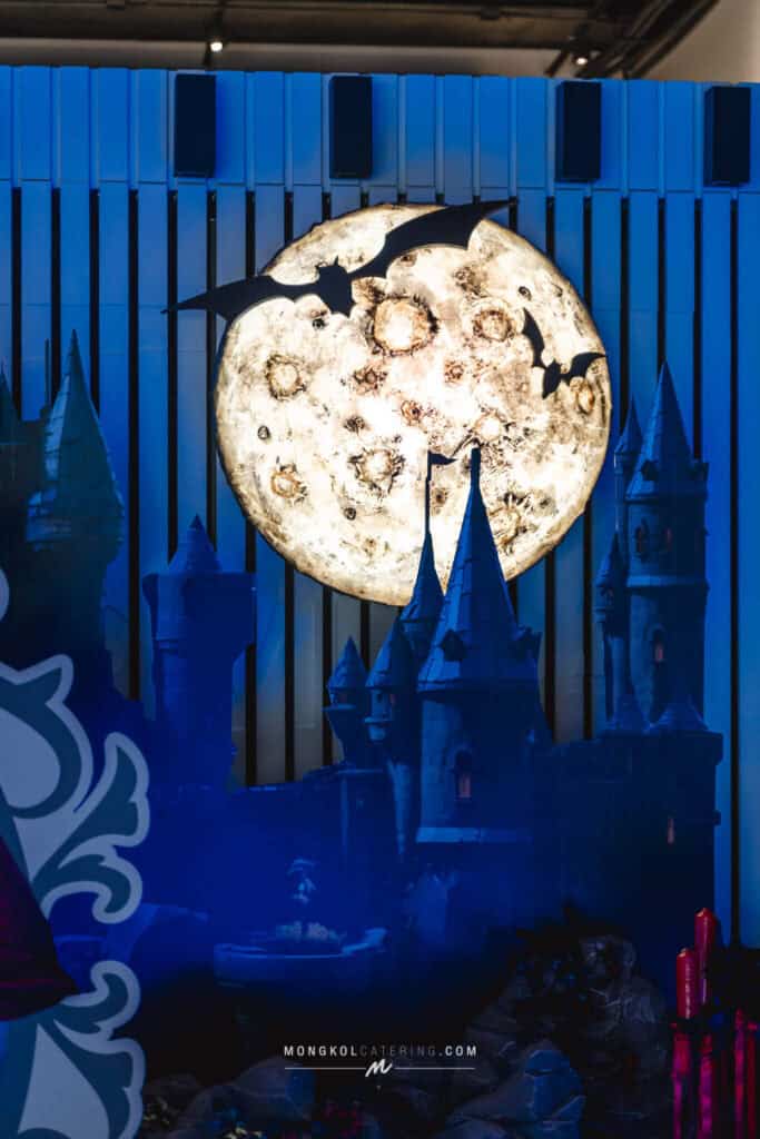 Giant illuminated moon with bats and haunted castle decor at Mongkol Catering event in Thailand.