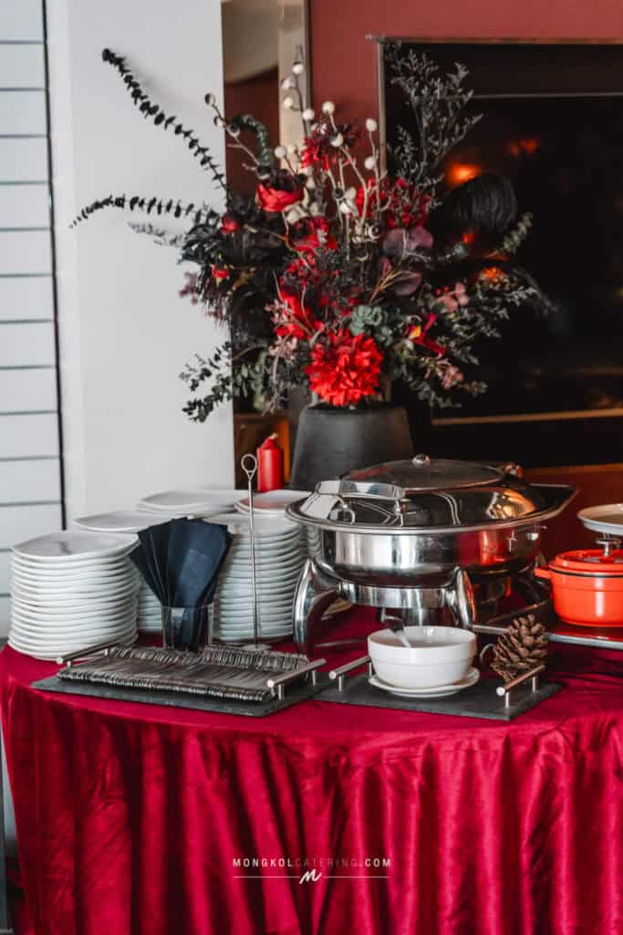 Elegant event catering setup with a floral centerpiece, white plates, and stainless steel chafing dishes in Thailand.