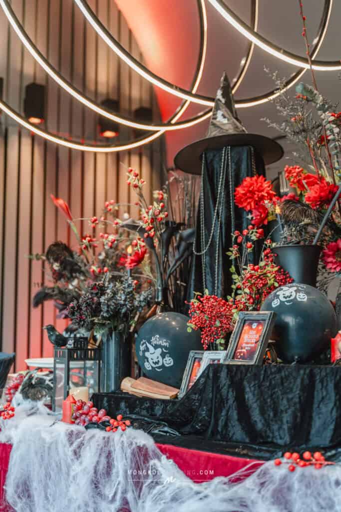 Ultra-modern Halloween-themed table setup with black pumpkins, red flowers, witch hat, and spooky decorations in Thailand.