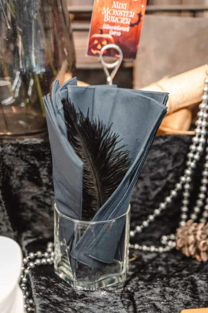 Black feather napkin in a glass holder at a Halloween-themed event in Thailand.