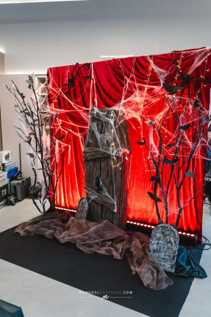 Spooky Halloween themed event decoration with red velvet curtains, cobwebs, bats, and tombstones in Thailand.
