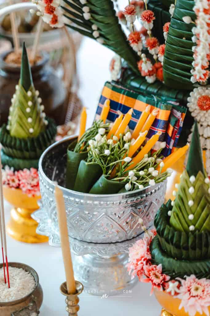 Colorful floral and candle arrangements for traditional Thai events with decorative banana leaf crafts.