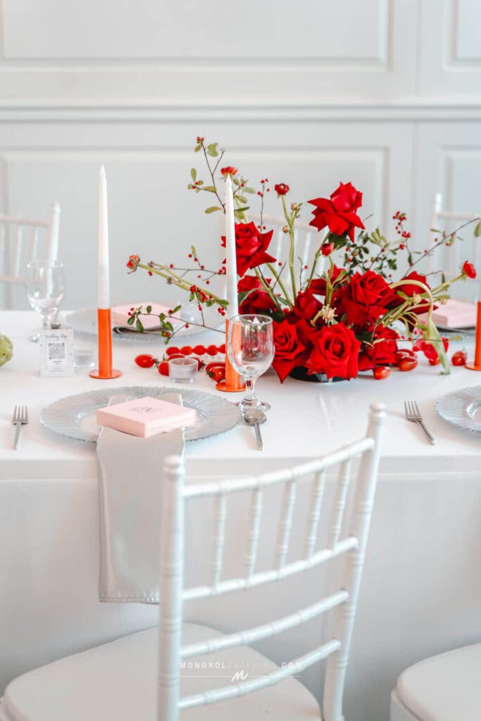 Vibrant red floral centerpiece for wedding reception with white table settings in Thailand.