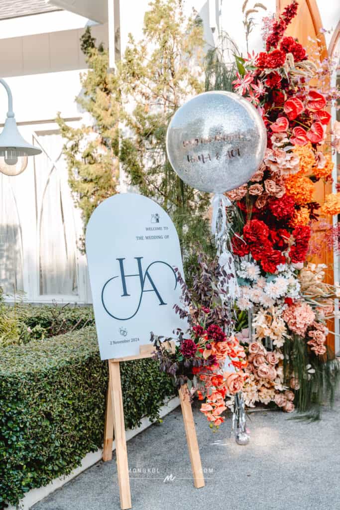Elegant wedding sign with floral arrangements at Mongkol Catering event in Thailand.