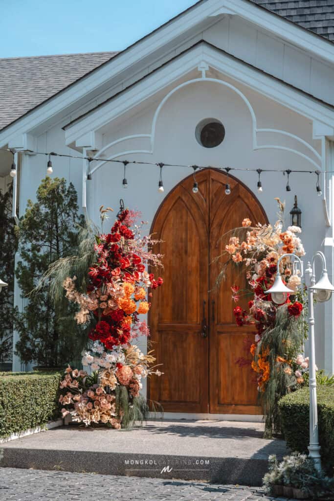 Colorful floral wedding arch decor in front of a white church in Thailand.