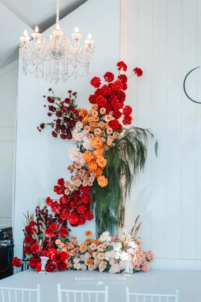 Vibrant wedding floral arrangement with red, pink, and orange flowers, elegant chandelier, perfect for events in Thailand.