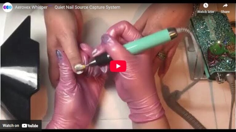 A person wearing pink gloves uses a green electric nail drill on another person's fingernail. A Whisper nail dust collector and decorated nail tool are visible nearby. The scene is a paused YouTube video about the Aerovex Whisper nail source capture system. Read more at Aerovex Systems (aerovexsystems.com)