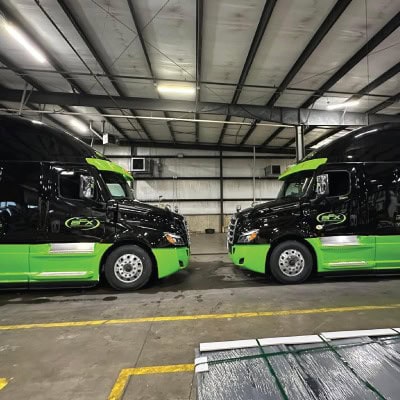 Two black and green freight trucks parked inside a warehouse.