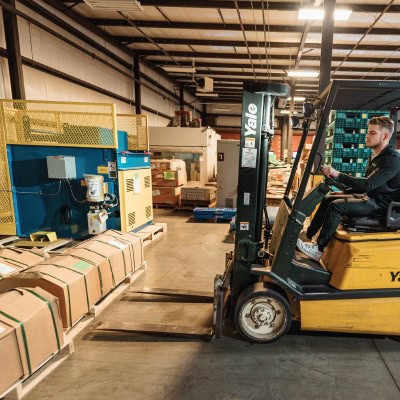 Warehouse worker using forklift to move boxes in a logistics warehouse.