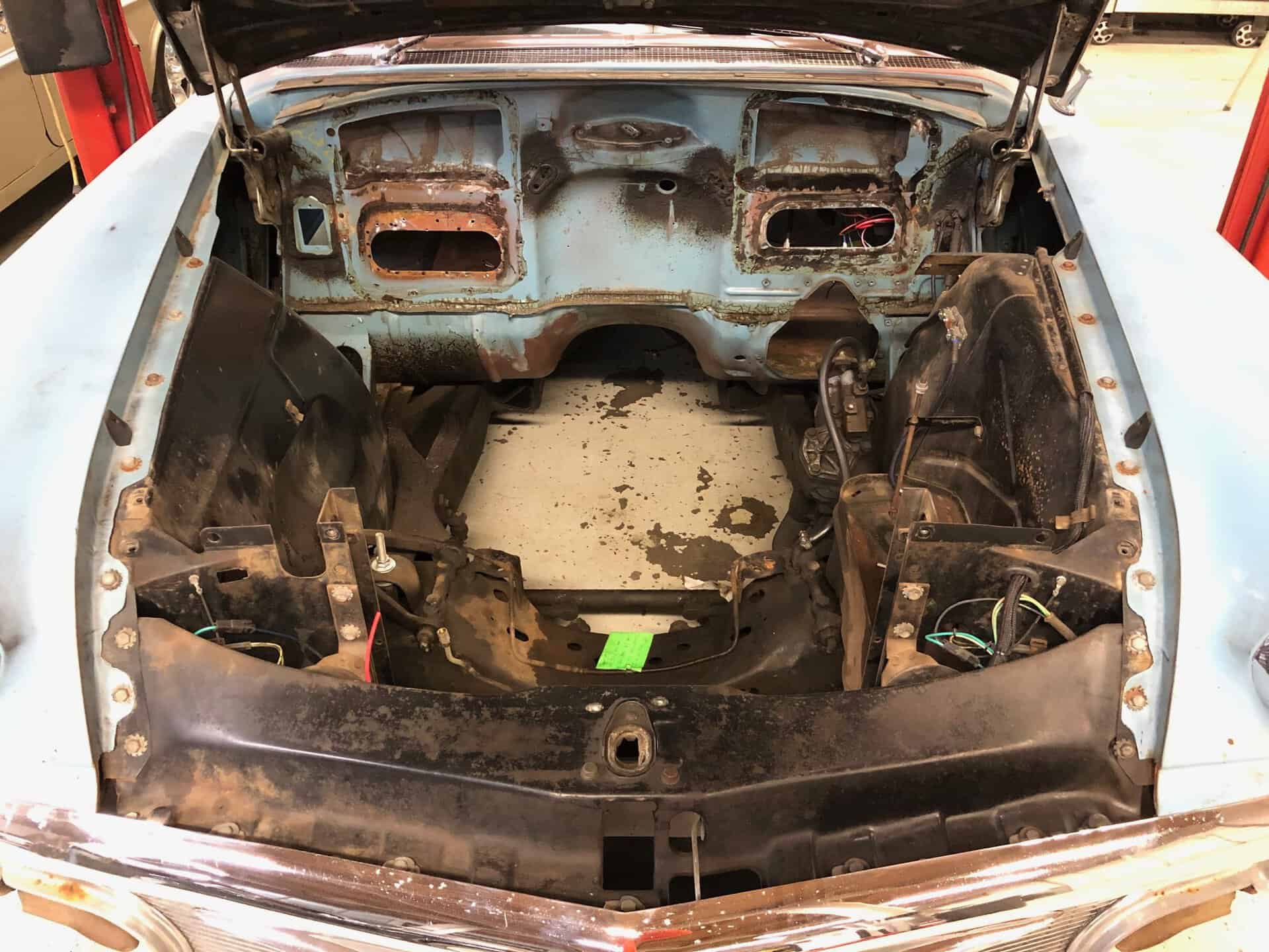 Bare metal car engine bay with rust and old wiring, ready for restoration or customization.
