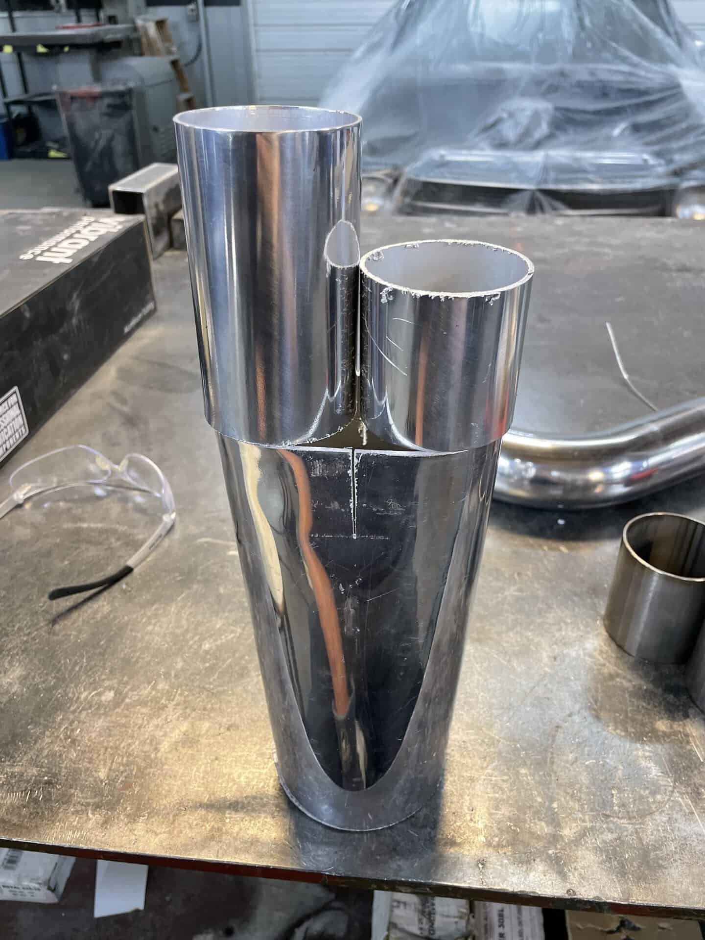 Polished chrome exhaust tip with dual outlets on workbench.