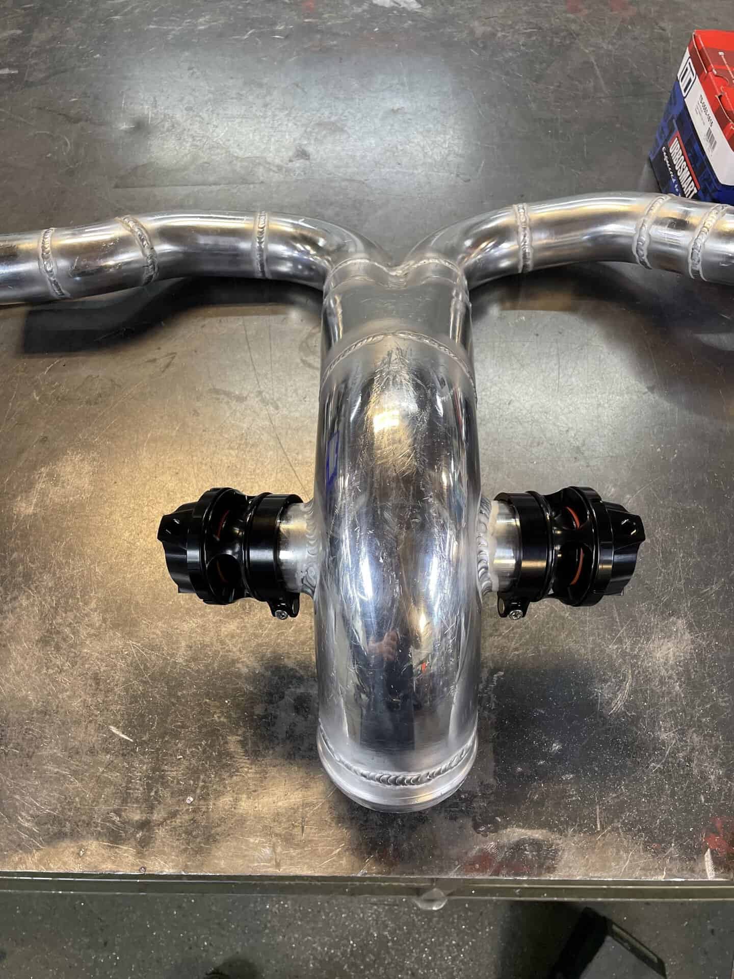Polished metal motorcycle handlebar with adjustable clamps on a workbench.