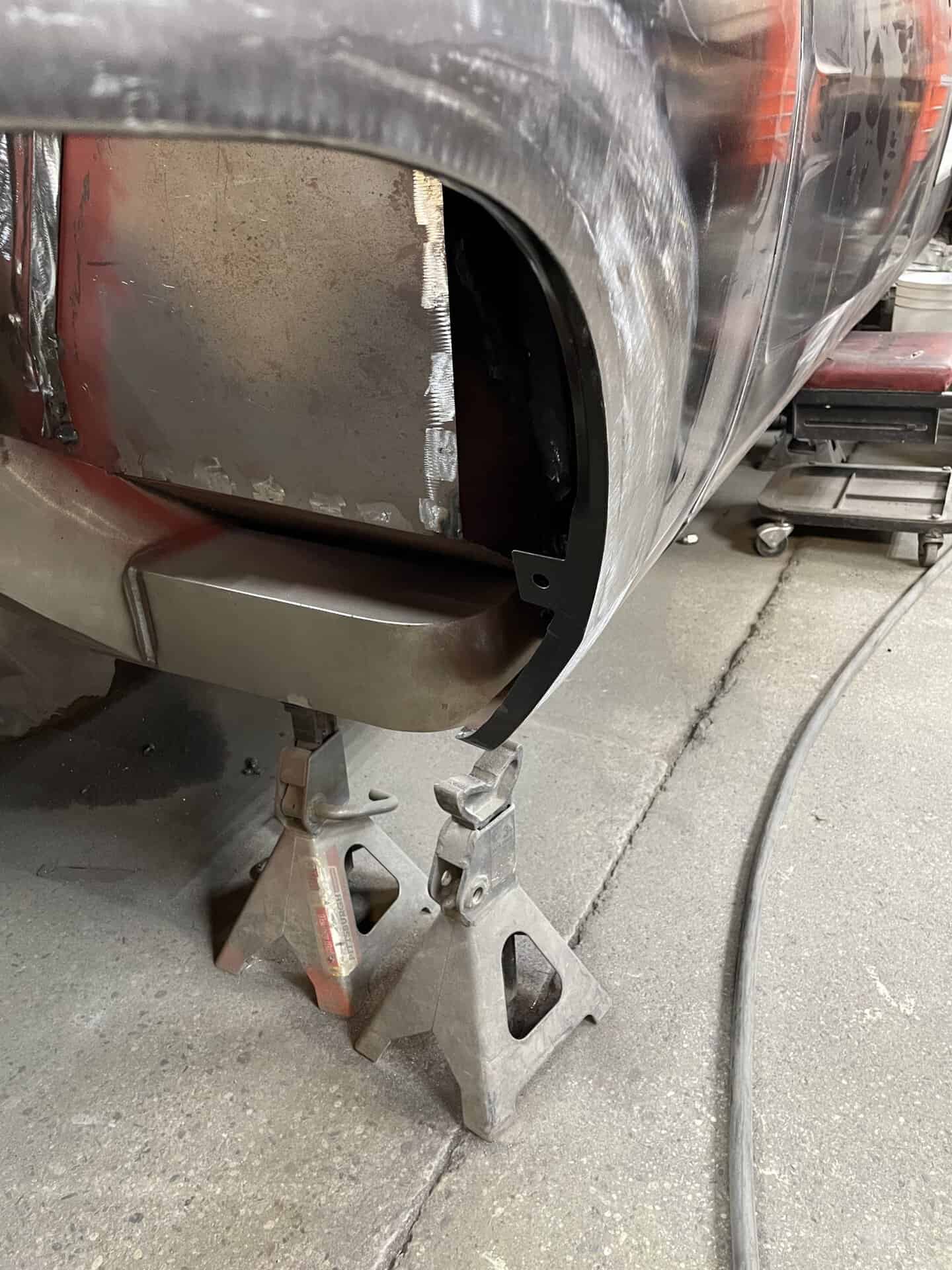 Car body repair with visible primer and sanding, on jack stands in workshop.