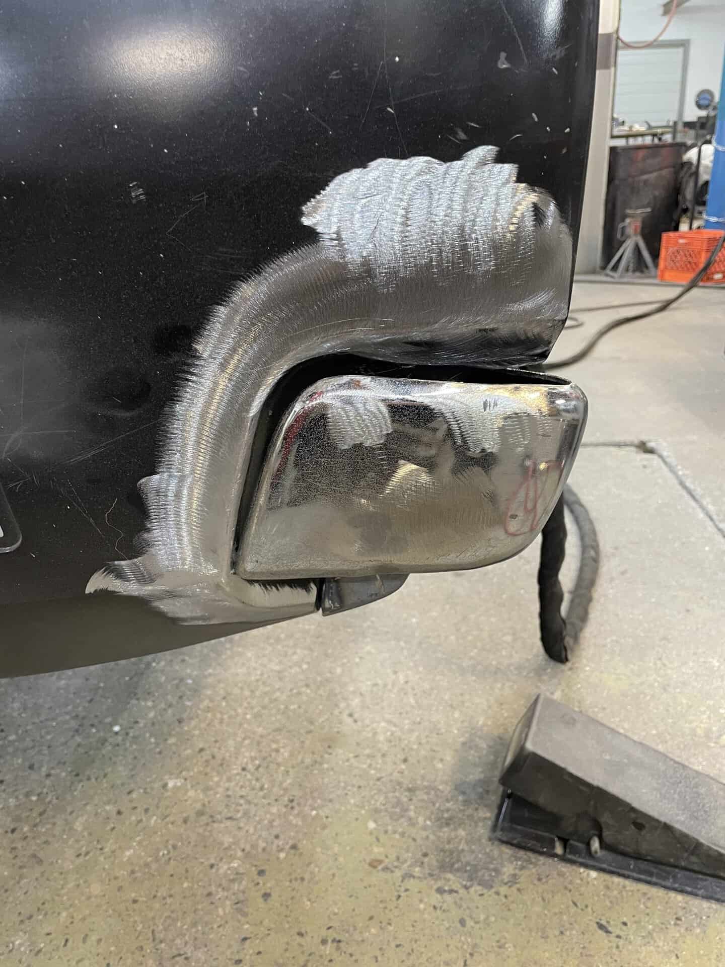 Welding repair on car bumper with visible weld bead and metal work.