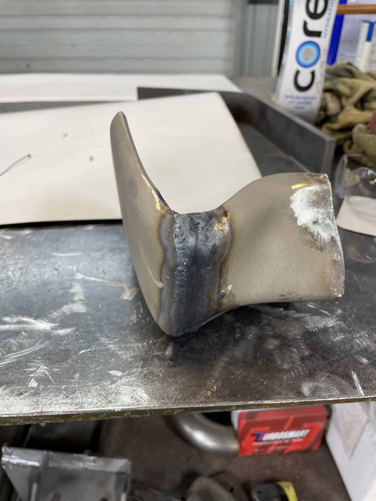 Welded metal car part on workbench in garage.