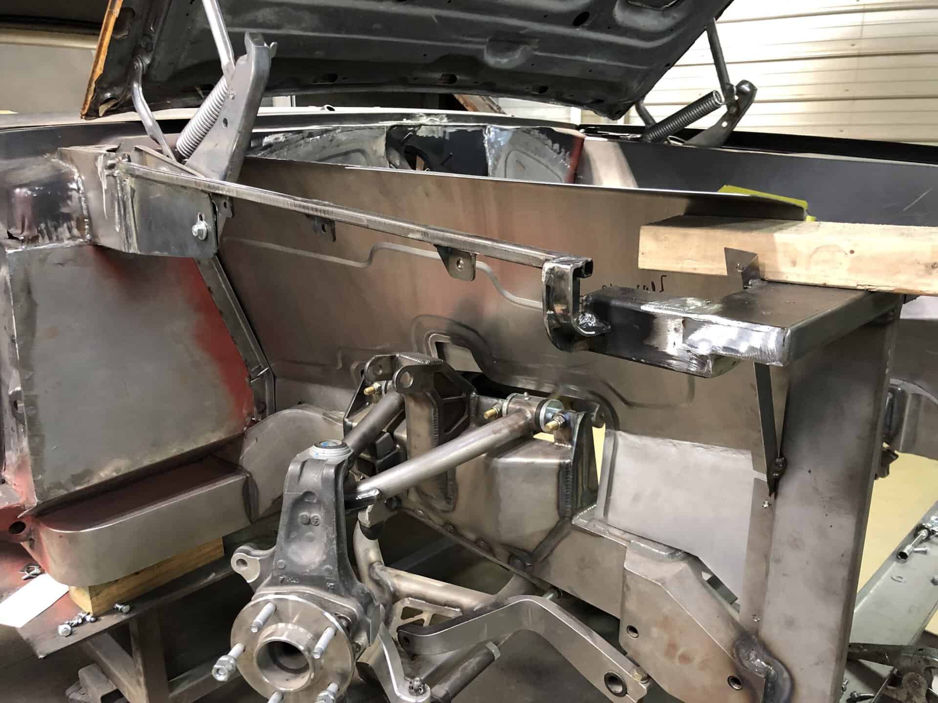 Car chassis with metal framework and engine components in workshop.