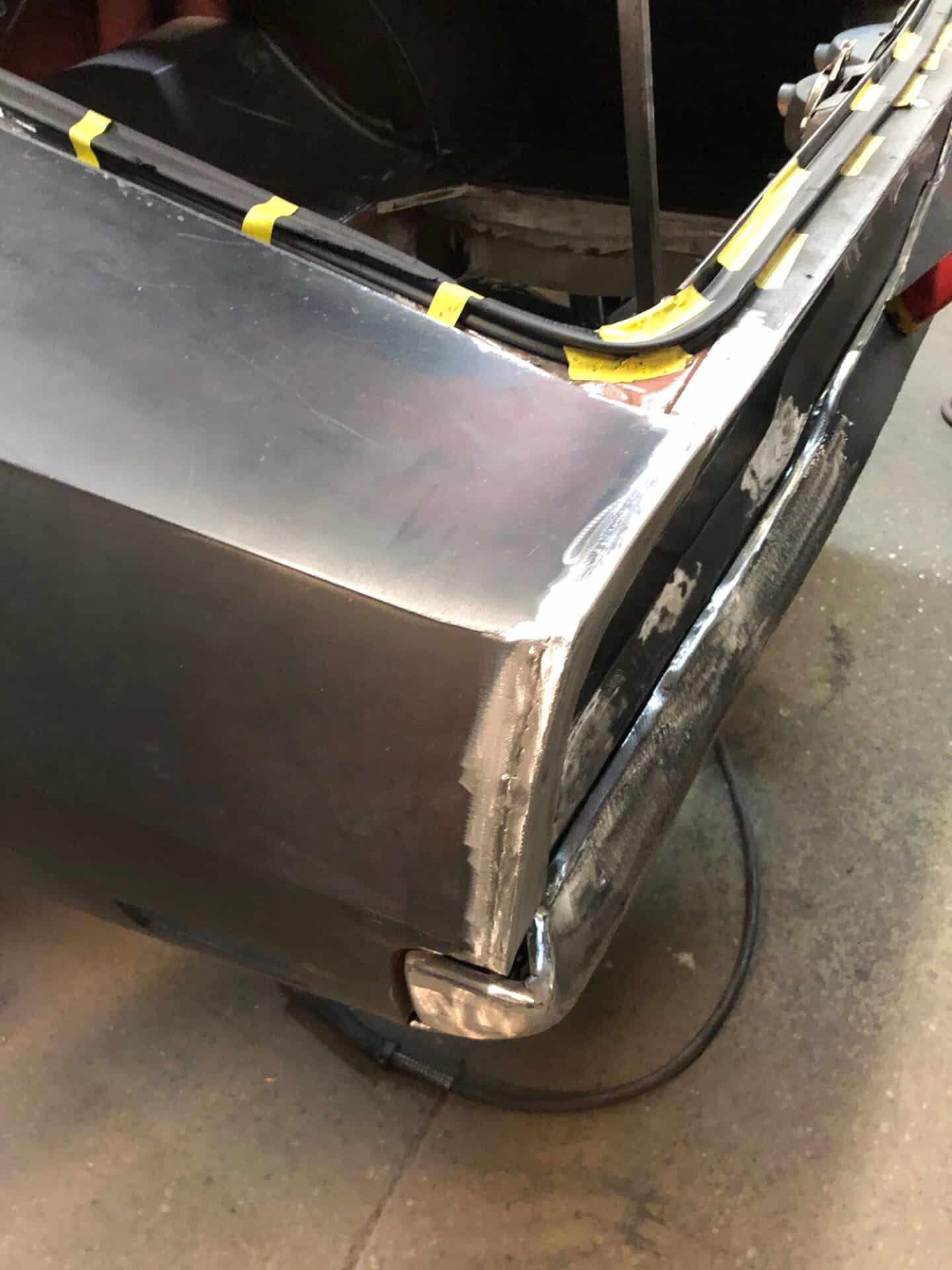 Close-up of a car's rear quarter panel being repaired with metal work.