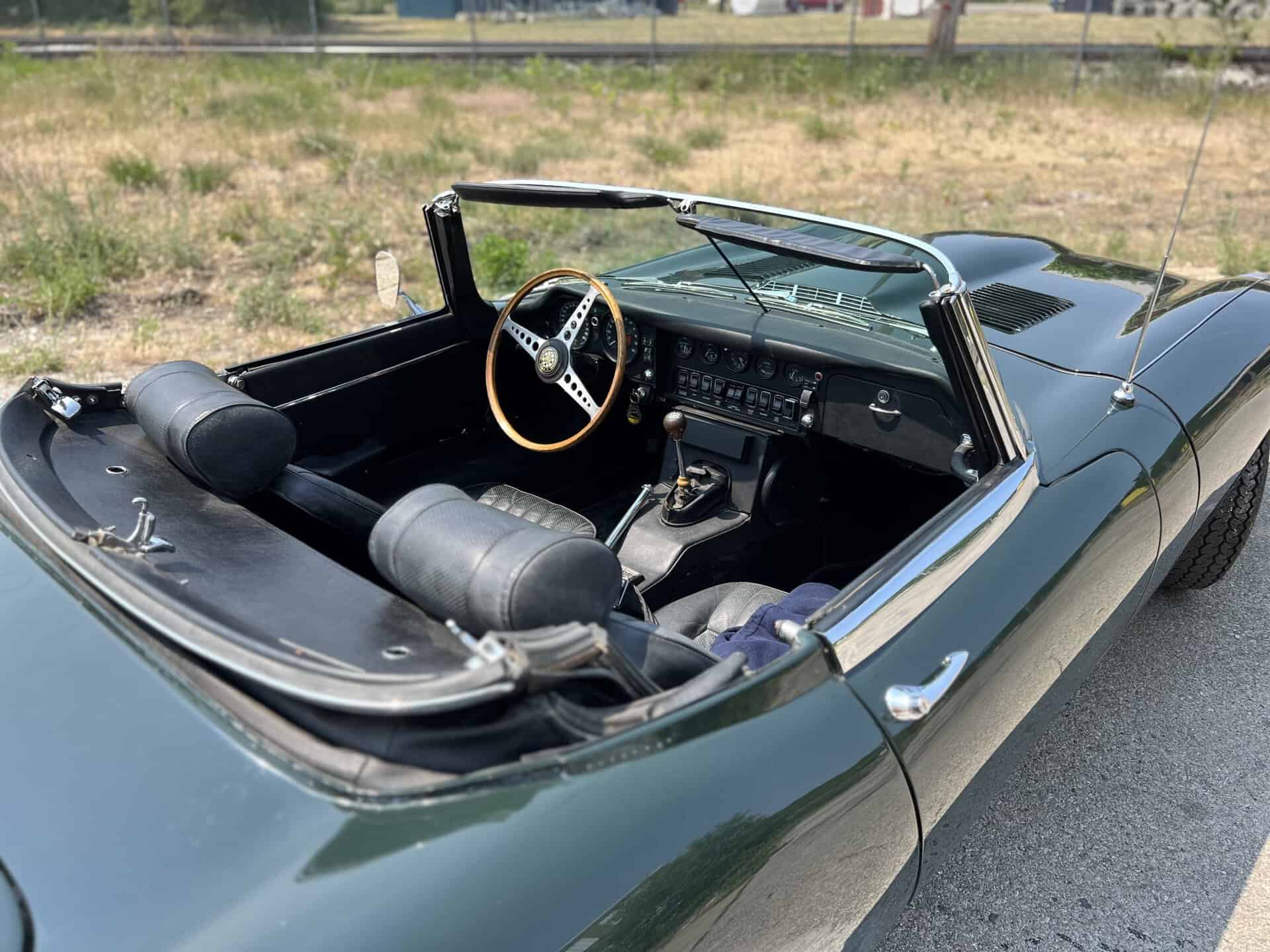Interior view of a 1970 Jaguar E-Type convertible with black leather seats and wooden steering wheel.