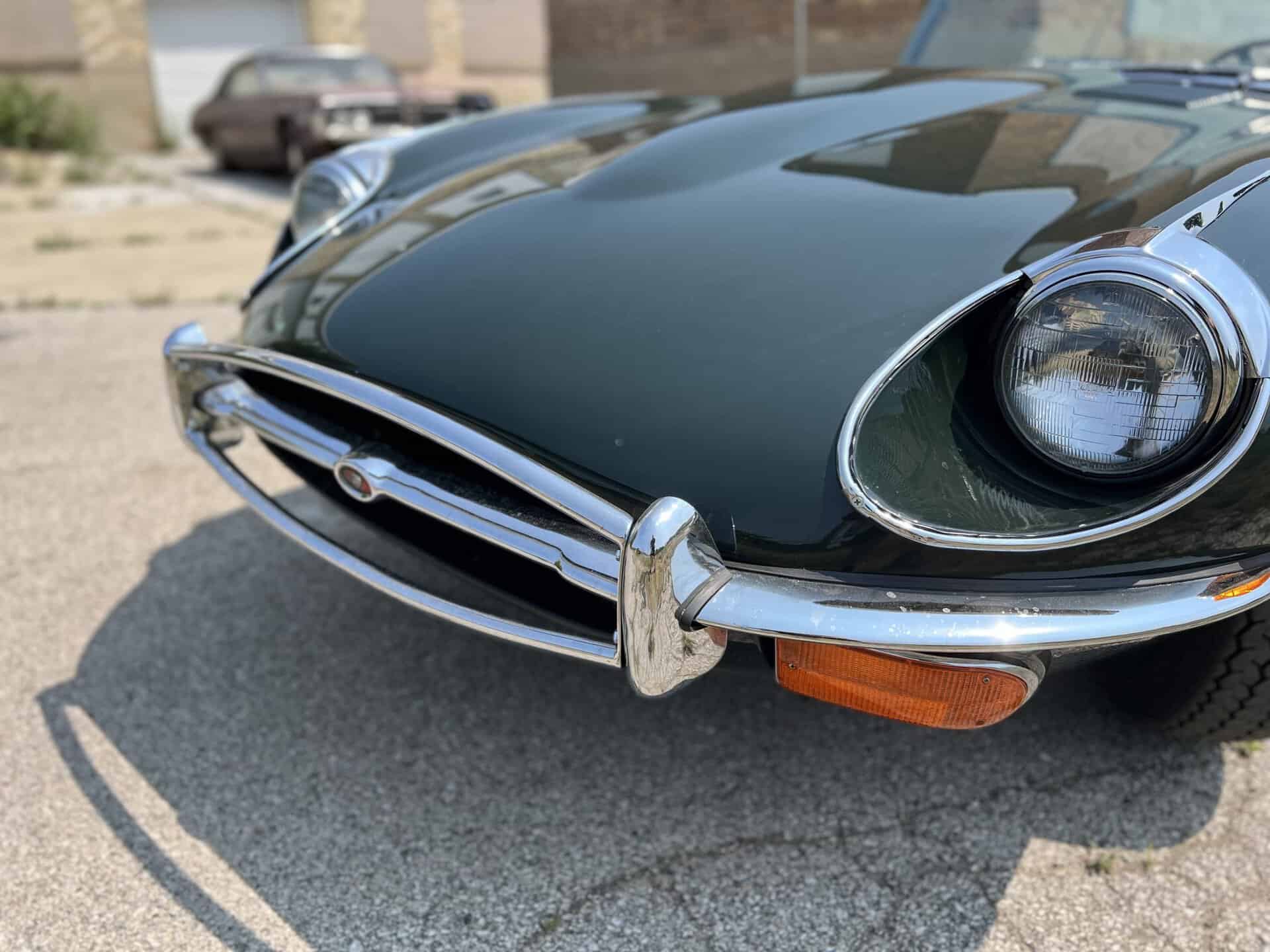 Close-up of the front of a 1970 Jaguar E-Type with chrome bumper and round headlight.
