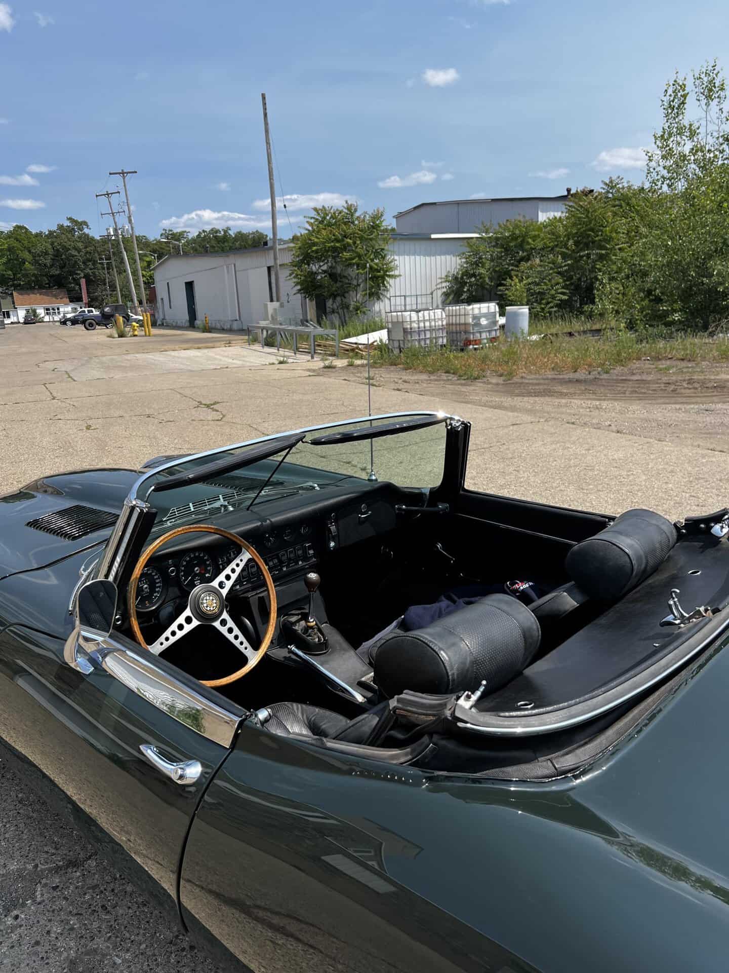Vintage Jaguar E-Type convertible with black interior and wooden steering wheel.