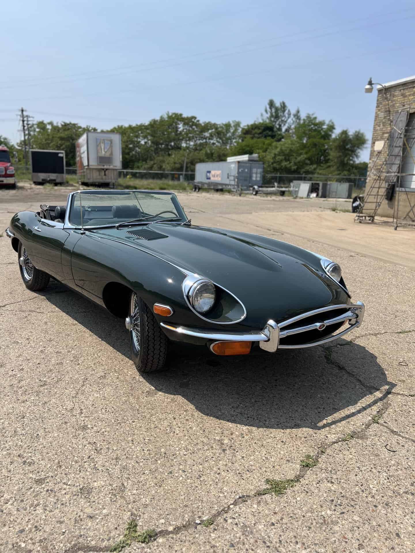 Classic 1970 Jaguar E-Type convertible in dark green parked outdoors.