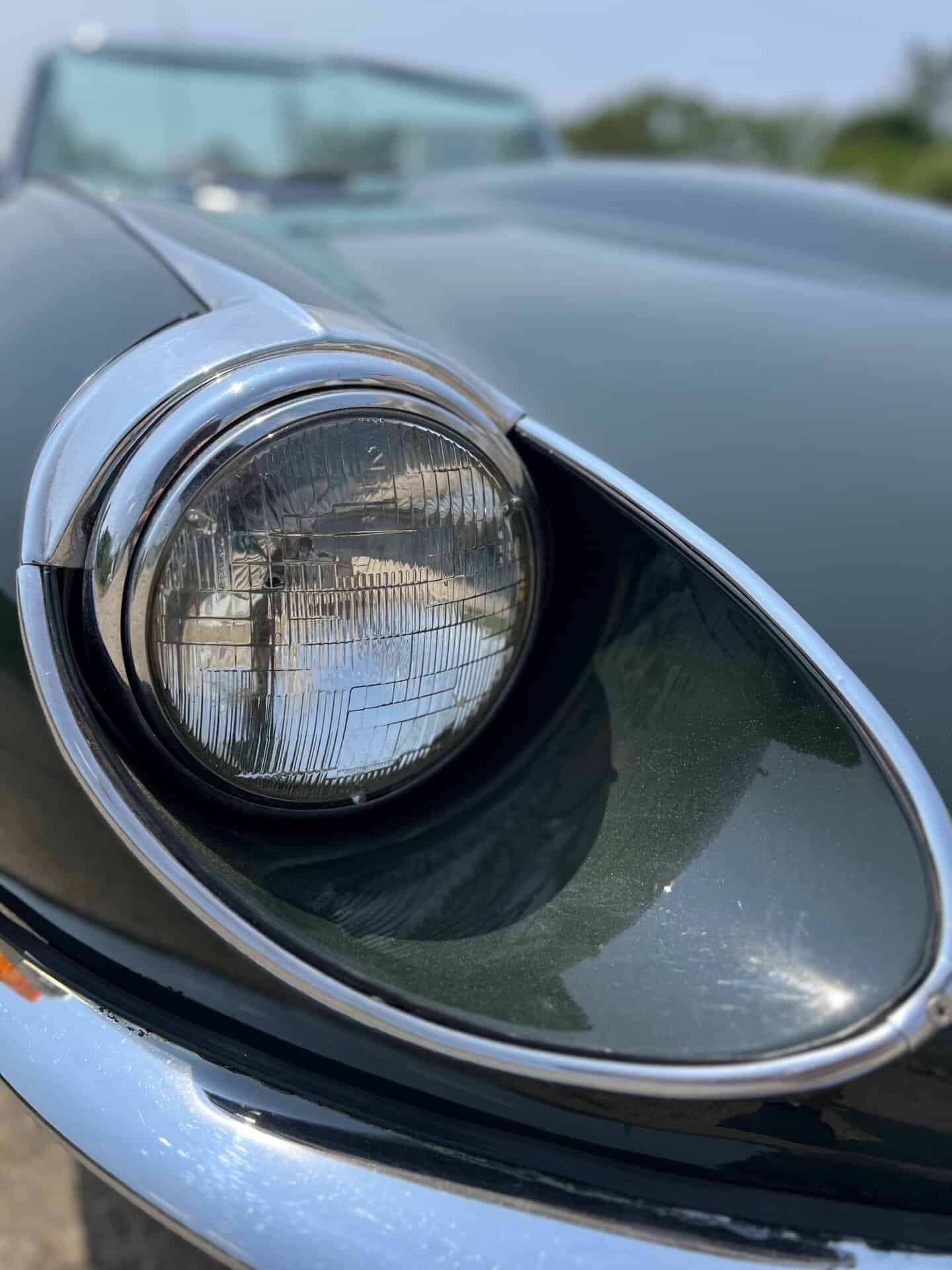 Close-up of a classic 1970 Jaguar E-Type headlight and front fender.
