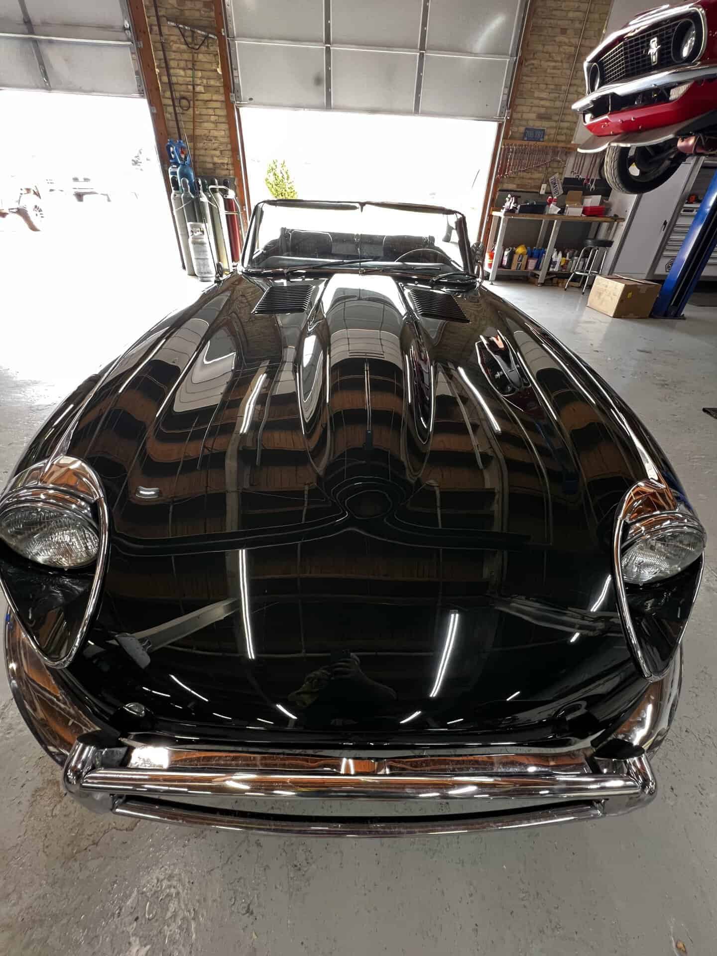 Black 1970 Jaguar E-Type in a garage with tools and car parts.