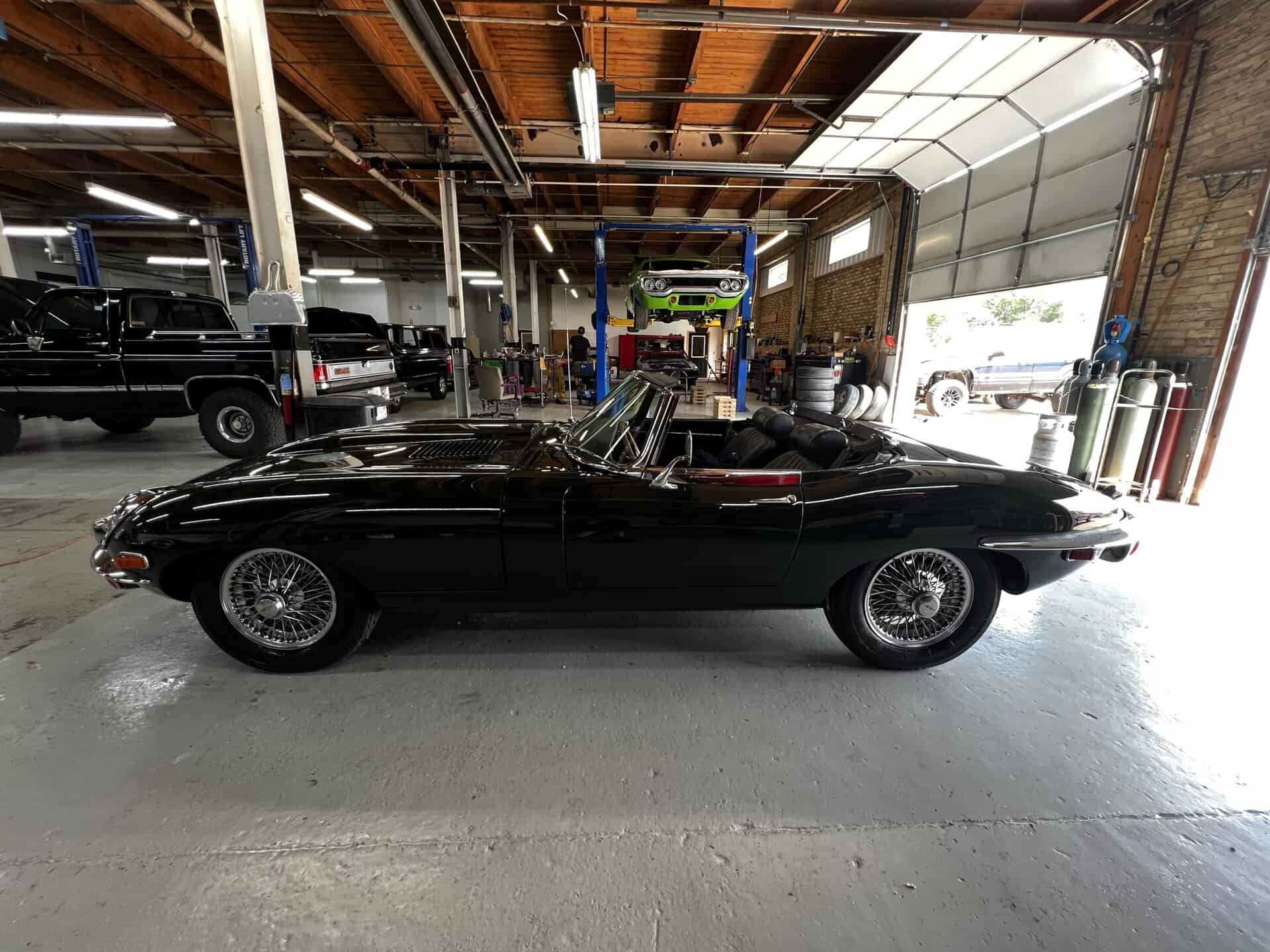 Black 1970 Jaguar E-Type convertible inside auto repair shop.