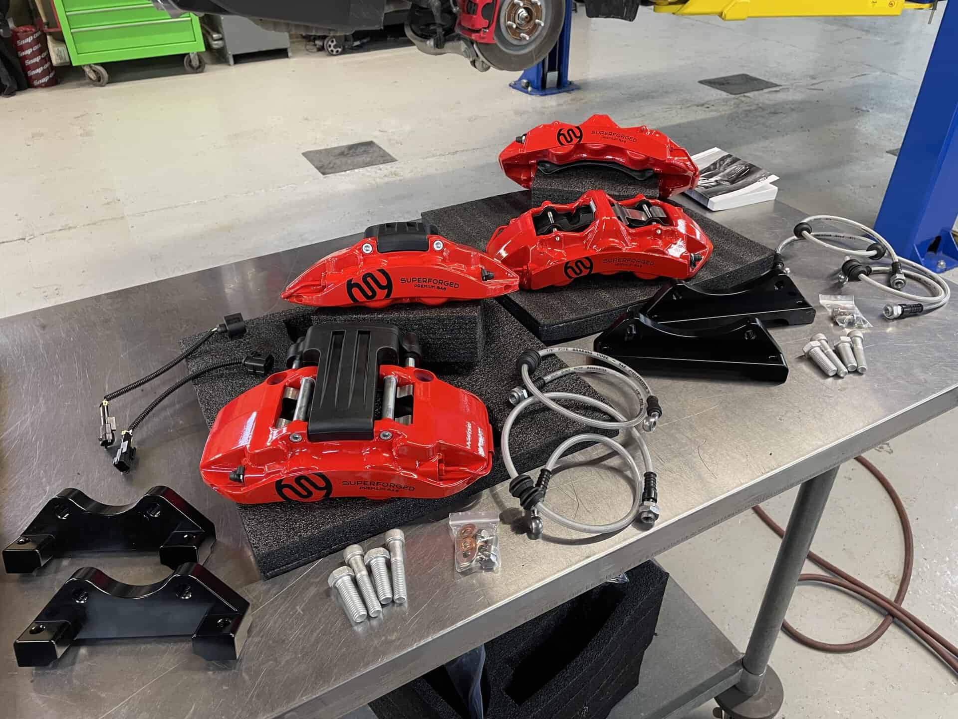 Red brake calipers with black accents and brake pads on a workbench.