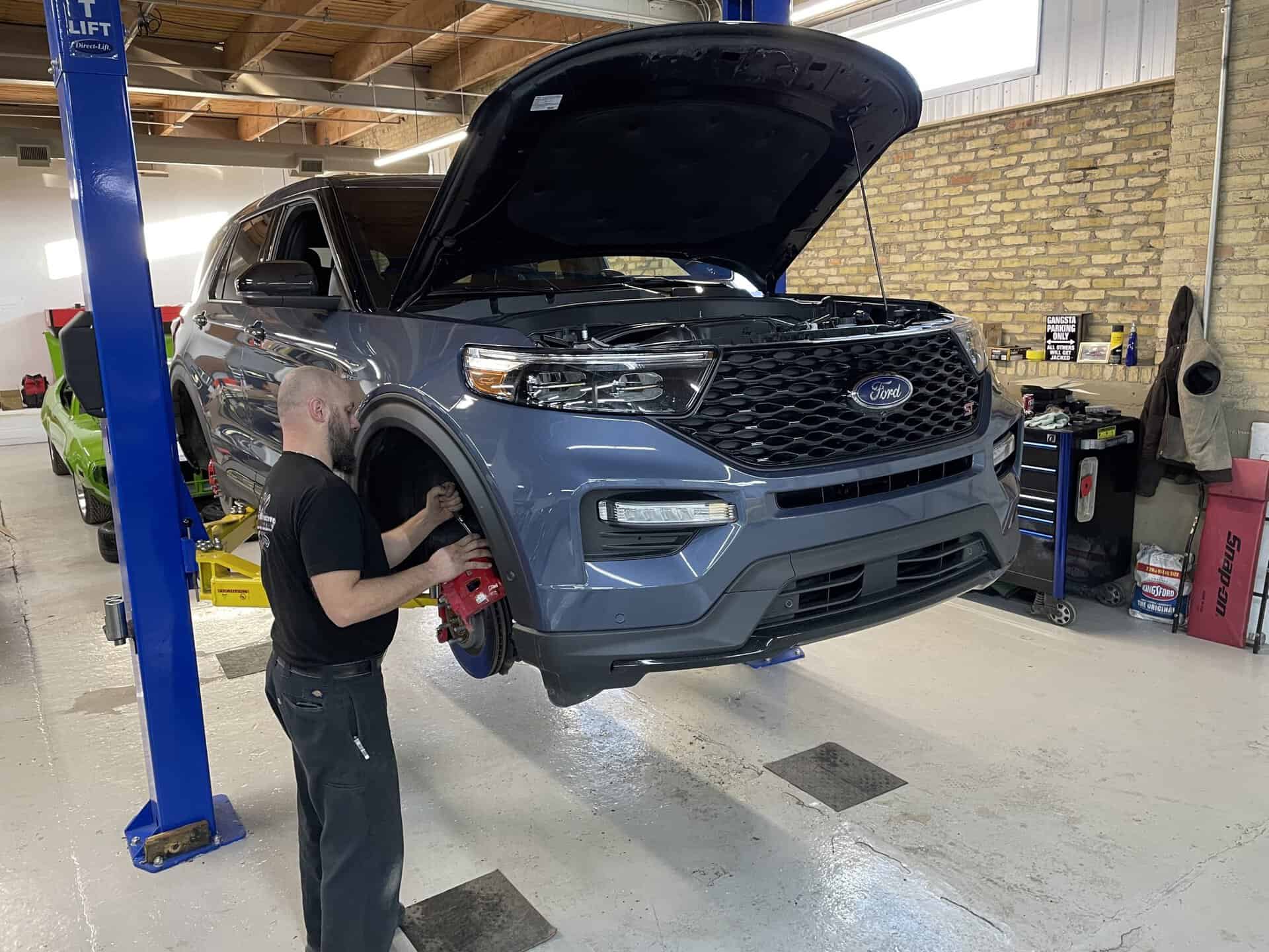 Mechanic inspecting the engine of a blue 2023 Ford Explorer Sport.