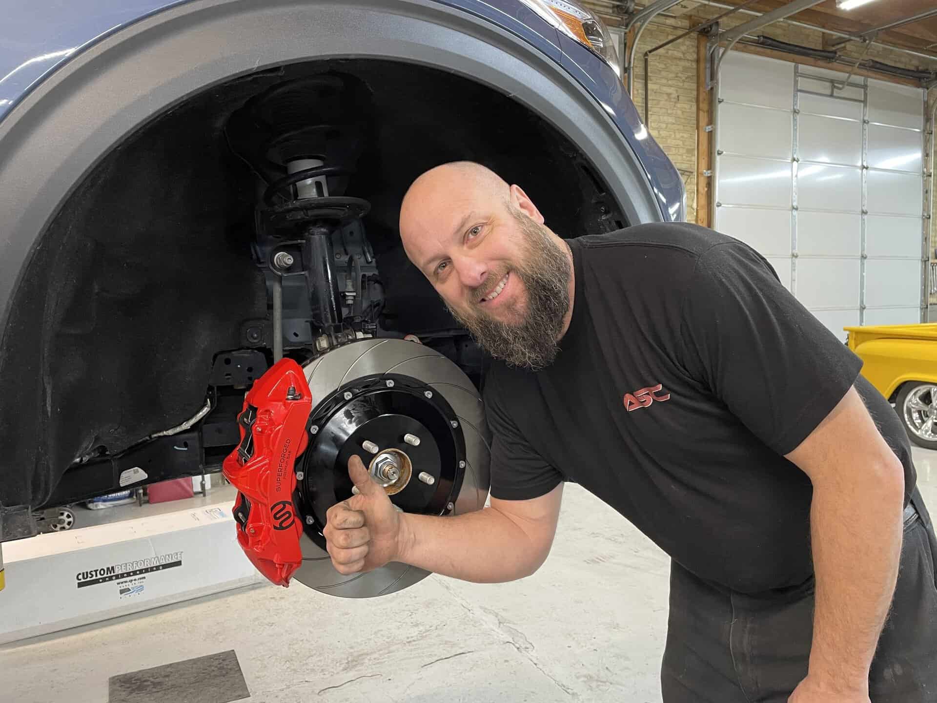 Technician inspecting red brake caliper on a vehicle.