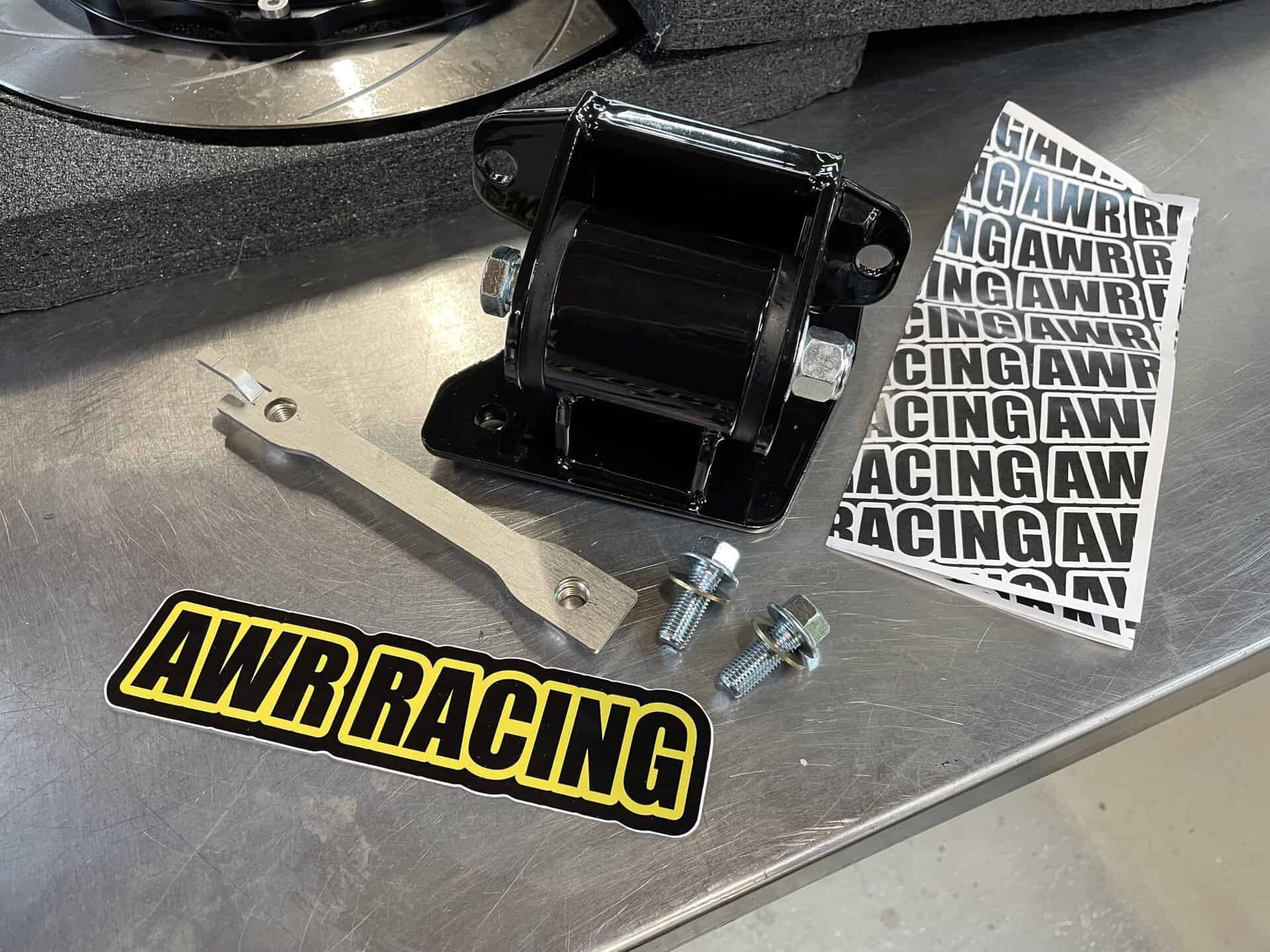 AWR Racing sticker with mounting hardware and black bracket on metal surface.