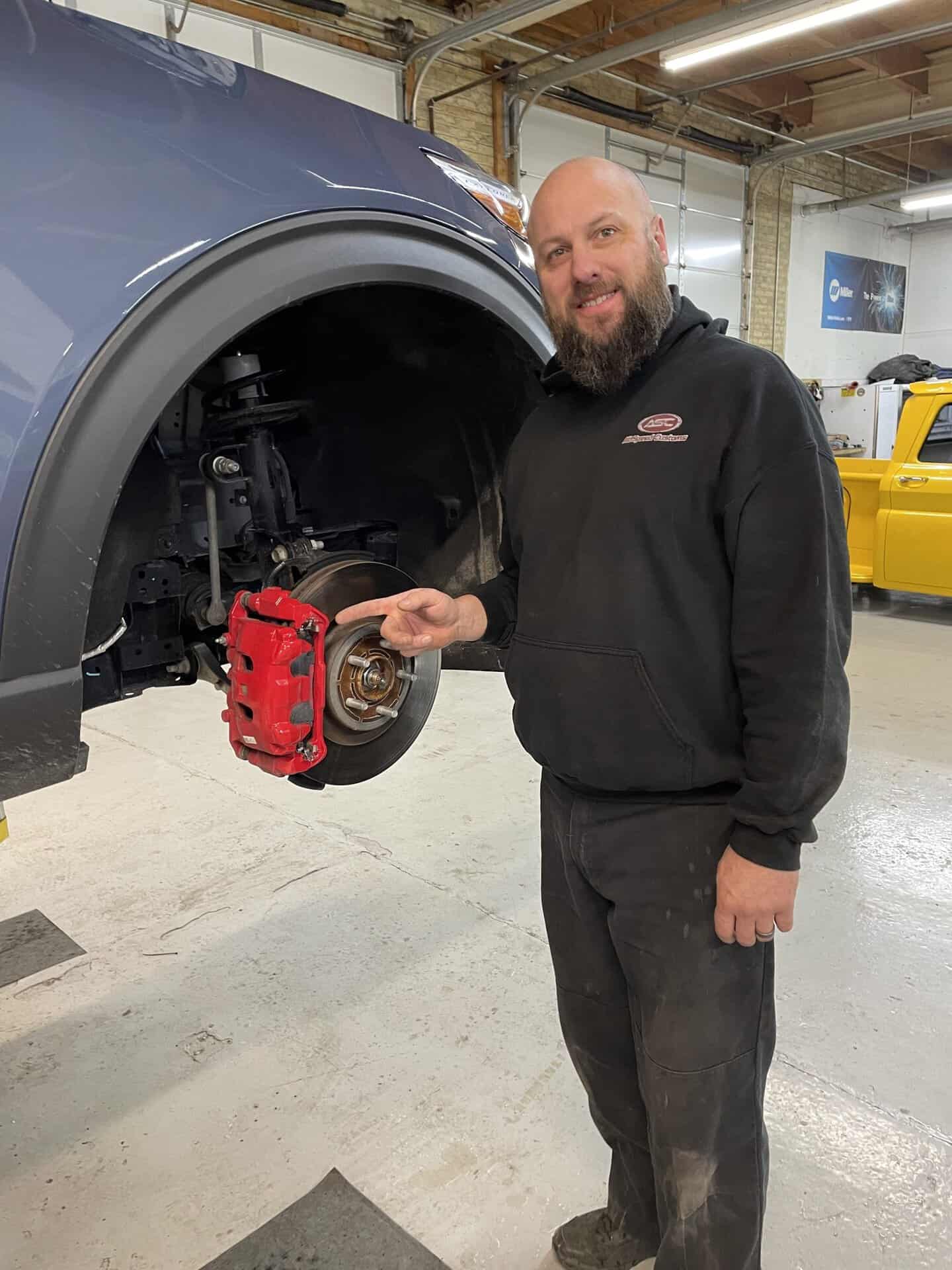 Technician inspecting brake system on a vehicle at All Speed Customs.