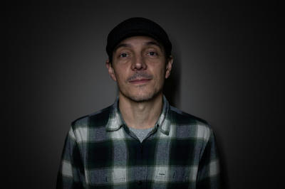 Man wearing a black cap and plaid shirt against a dark background.