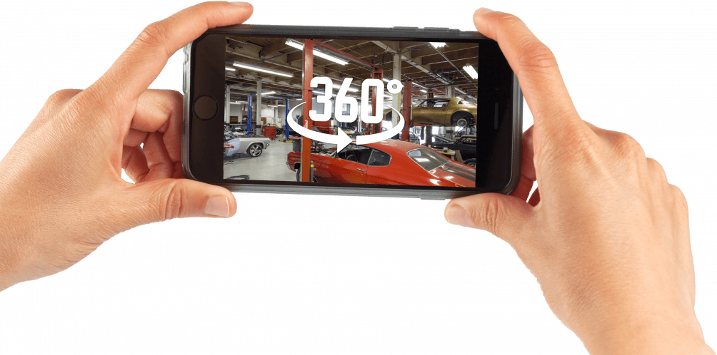Hands holding smartphone showing 360-degree view of a car in a showroom.
