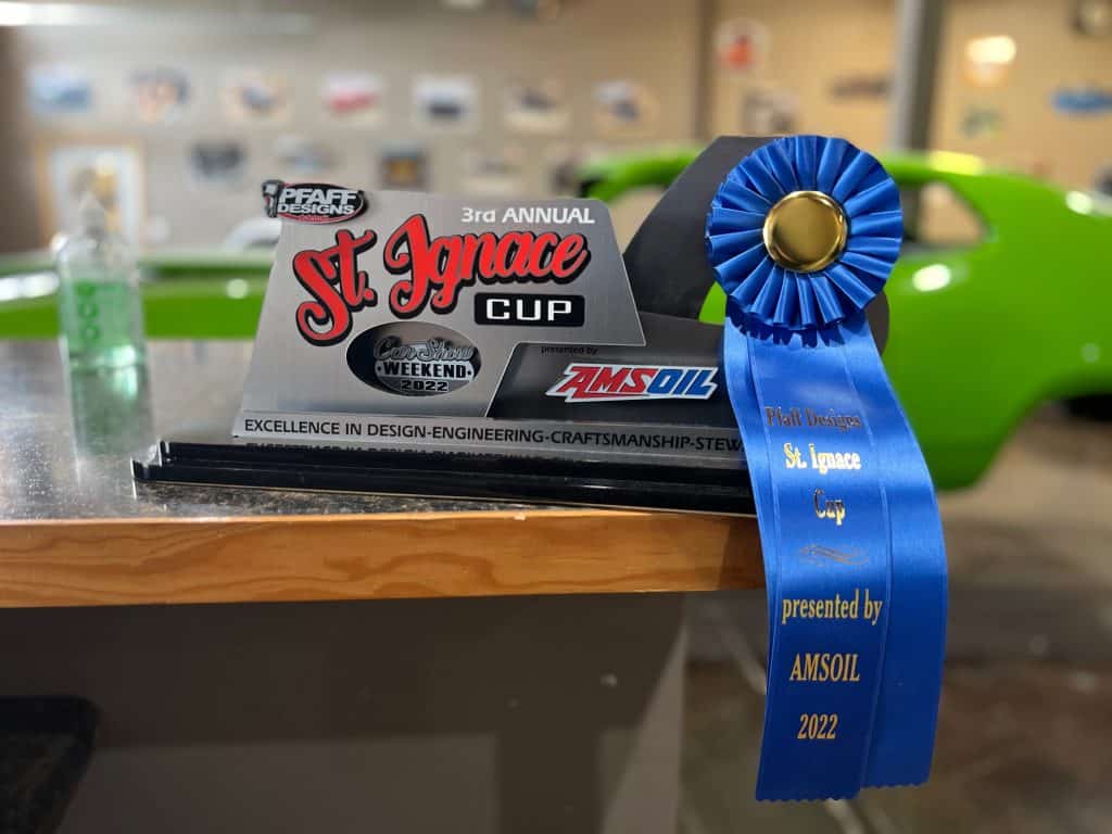 St. Ignace Cup award trophy with blue ribbon and car in background.