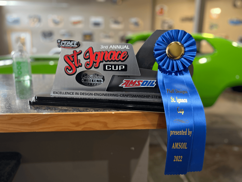 St. Ignace Cup award trophy with blue ribbon and car in background.