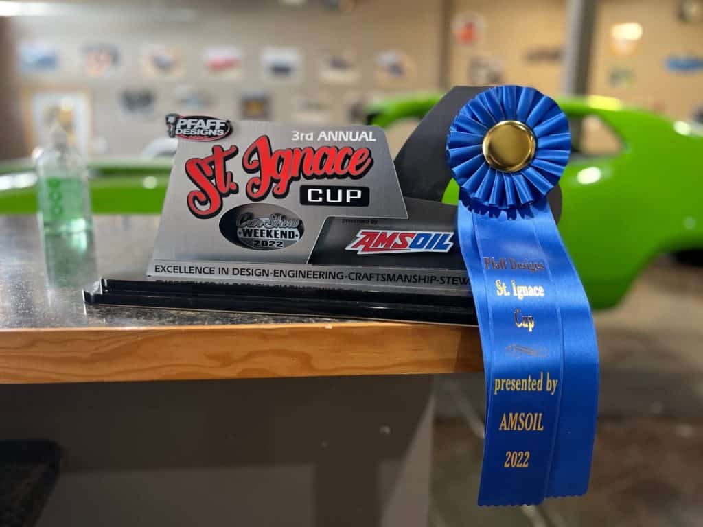 St. Ignace Cup award with blue ribbon and car in background.