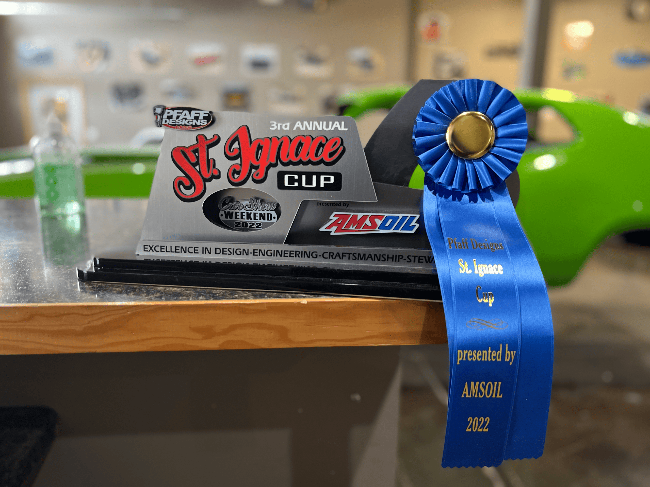 St. Ignace Cup award trophy with blue ribbon and car in background.