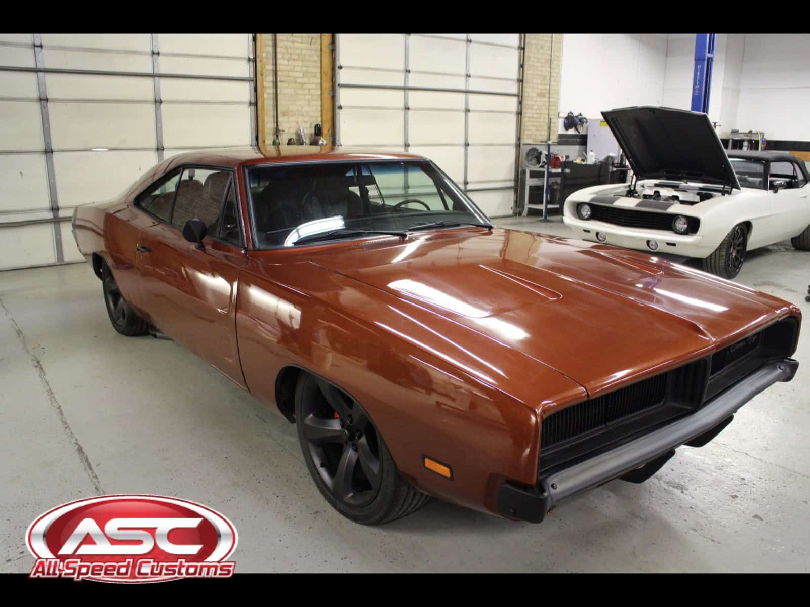 Brown 1968 Dodge Charger with black wheels inside workshop.