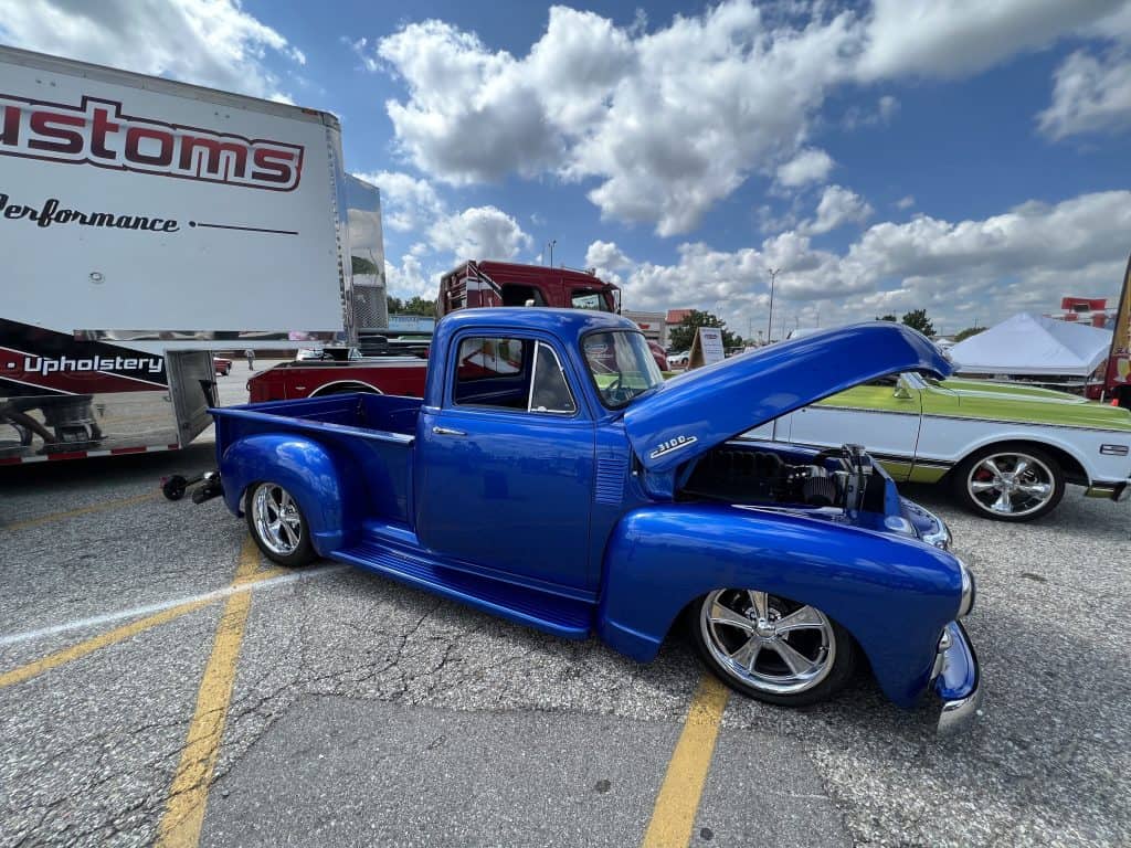 Blue custom vintage pickup truck with open hood at car event.
